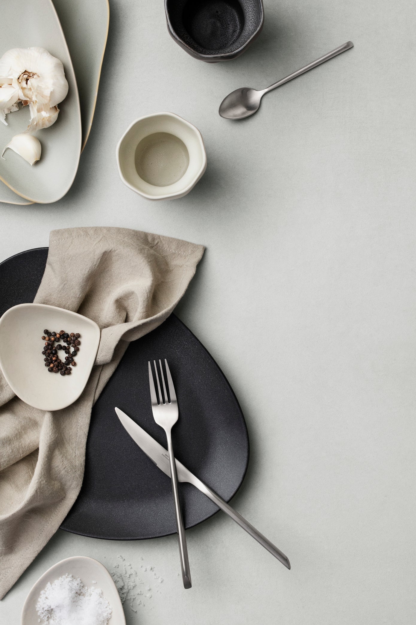 Table setting with black plates, silver cutlery, and neutral napkin on a light gray surface.