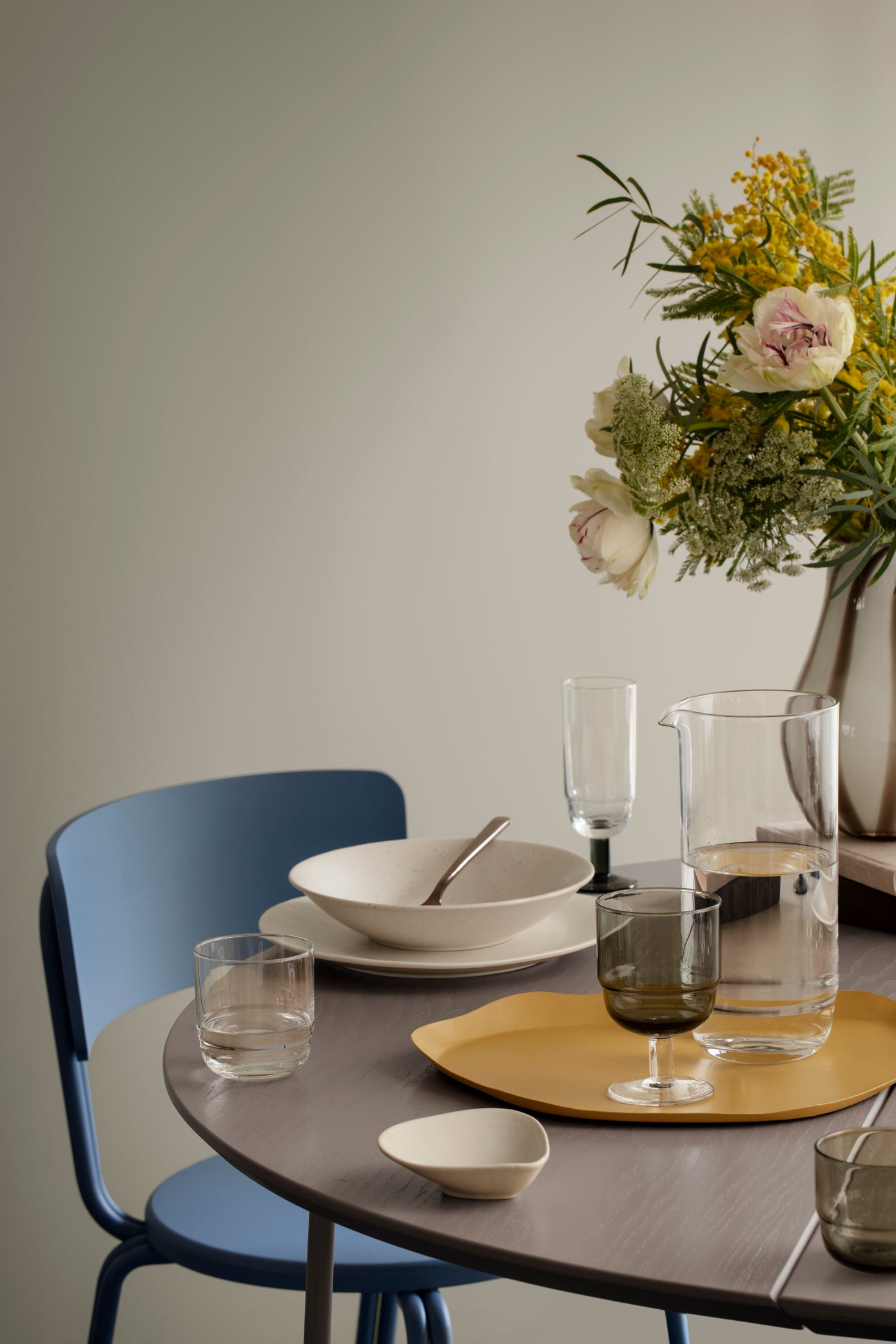 Dining table setting with plates, glasses, and a vase of flowers on a neutral background