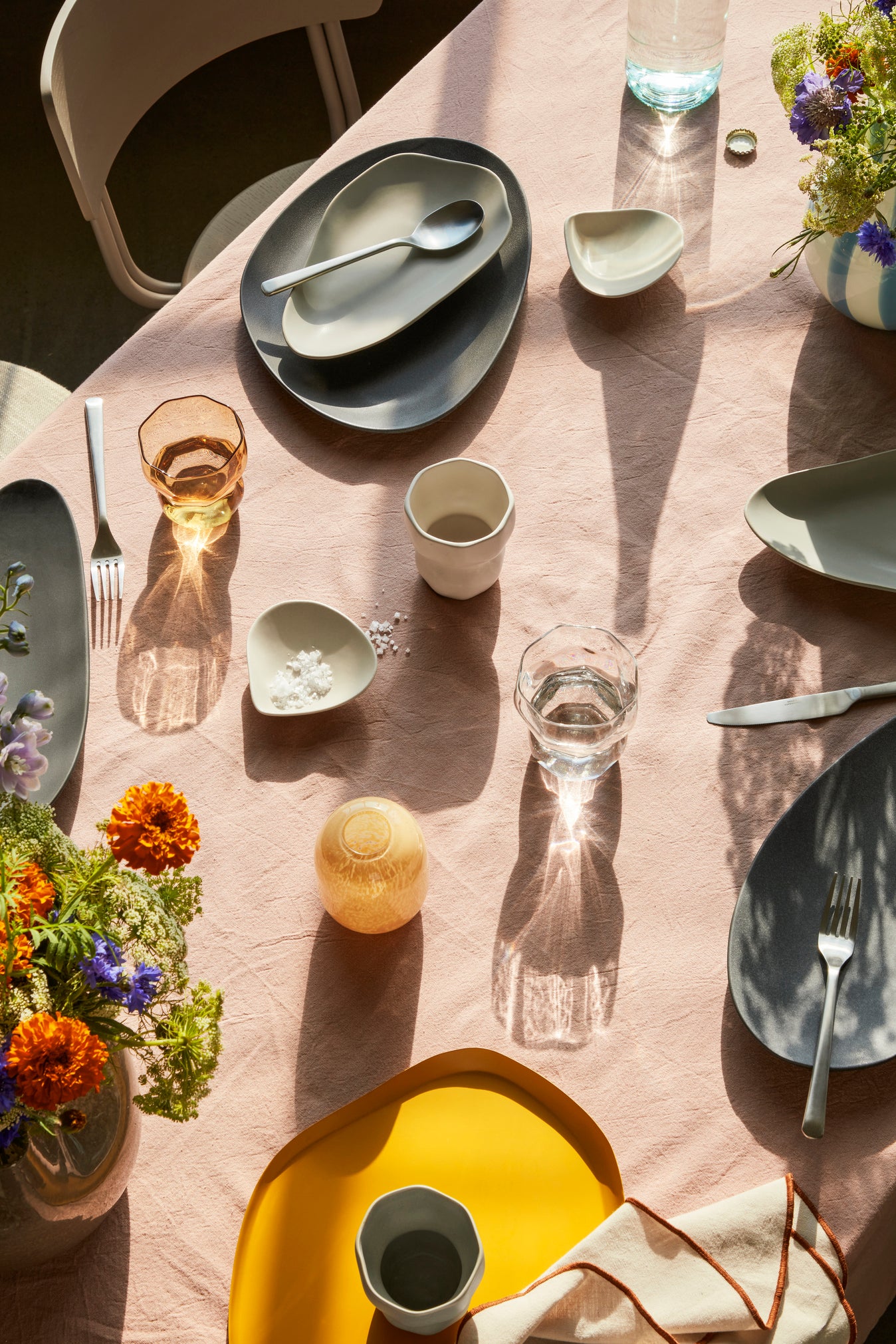 Elegant table setting with plates, cups, and flowers on a light pink tablecloth.