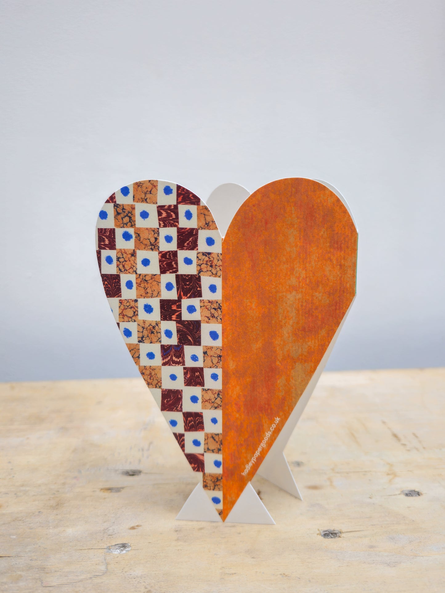 Back view of heart-shaped card with checkered pattern and rust colour finish on a wooden surface.
