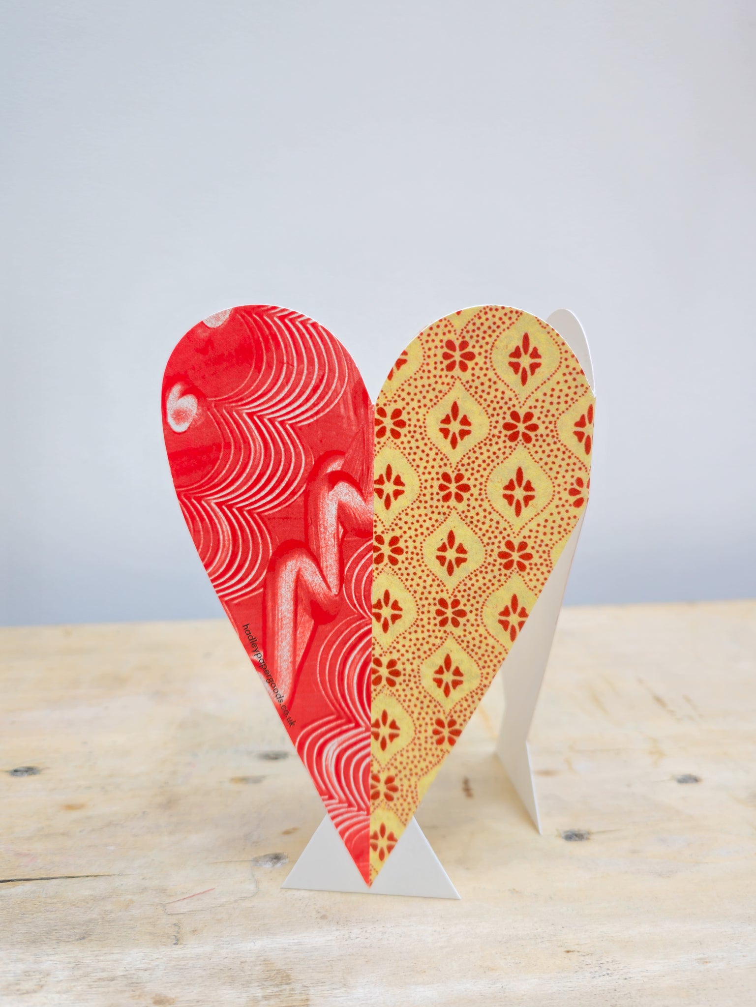Heart-shaped card with red and yellow patterns on a wooden surface.