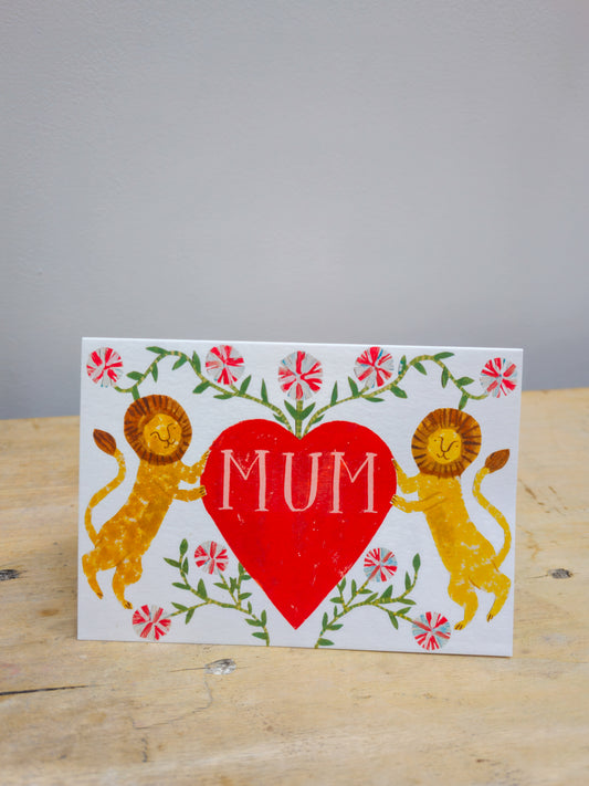 Card with two lions holding a red heart with 'MUM' text on a wooden surface.