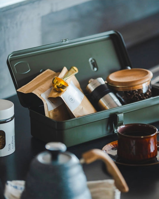 Open toolbox with kitchen items including a knife, container, and pot on a dark surface.
