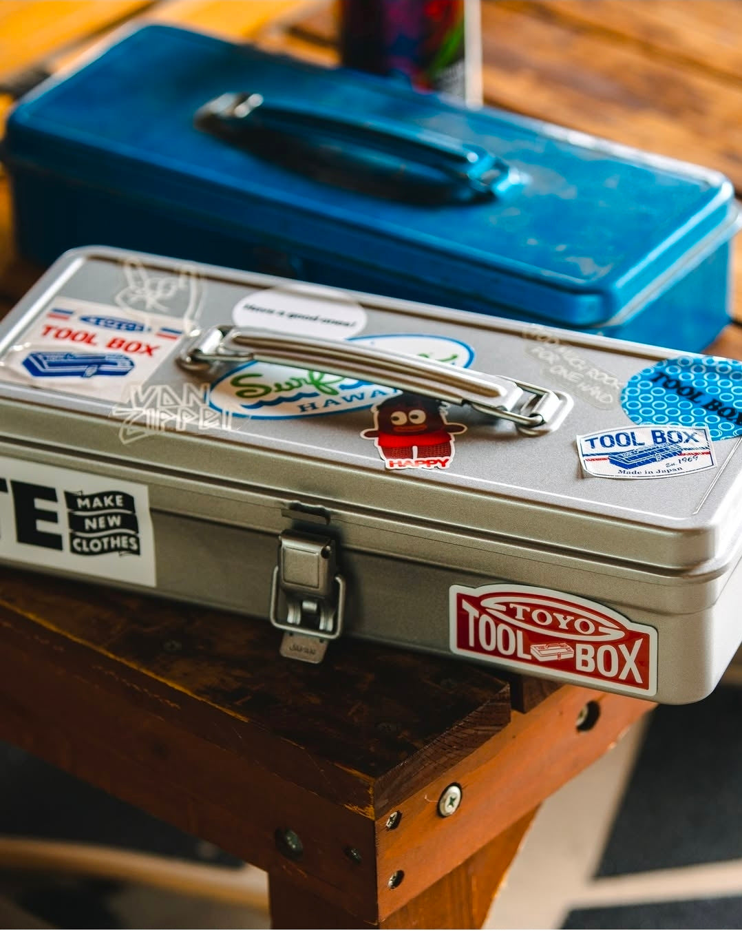 Metal toolbox with various stickers on a wooden surface