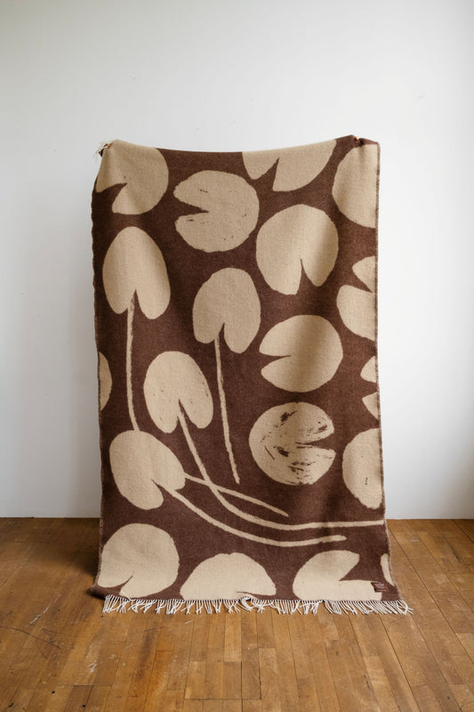 Brown blanket with beige floral pattern on a wooden floor against a white wall