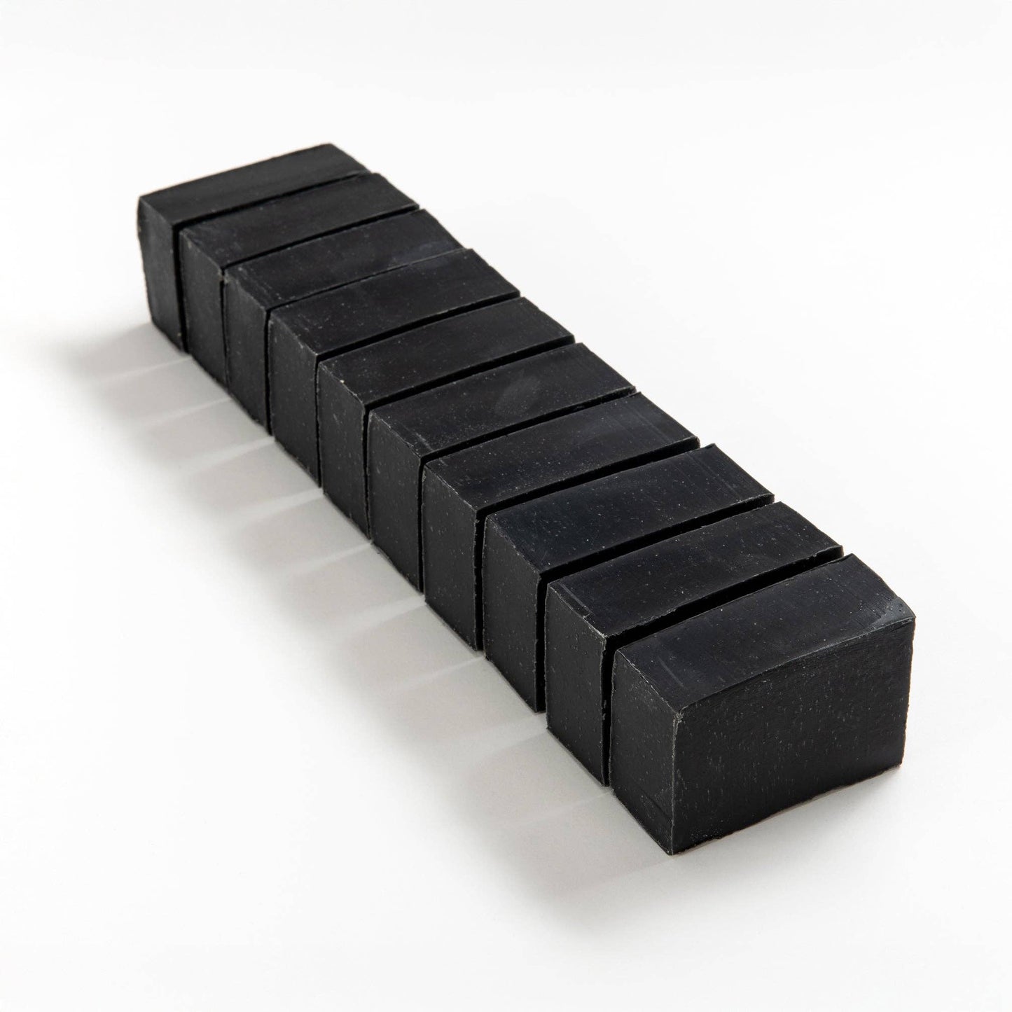 Row of activated charcoal soap brick cut into smaller pieces on a white background.