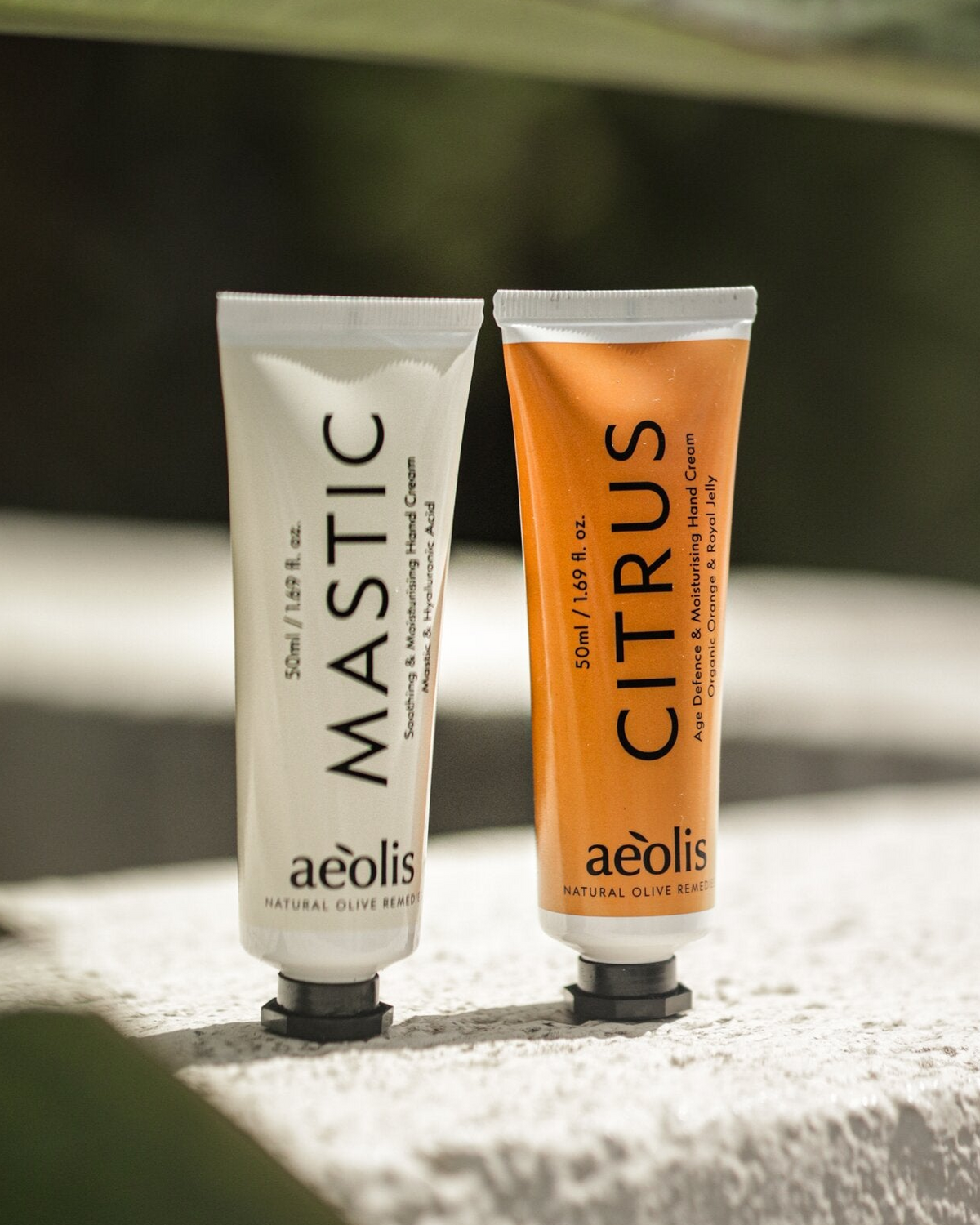 Aeolis mastic and citrus hand creams standing on pale stone among leaves