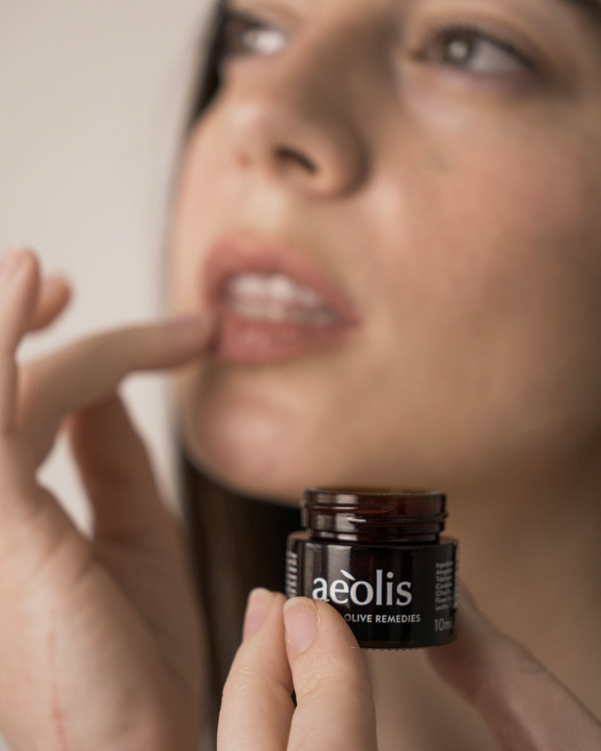 Woman holding a jar of Aeolis repair lip balm near her lips