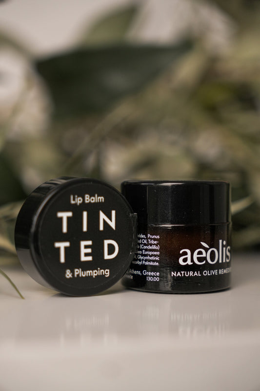 Aeolis tinted lip balm jar beside its lid with green leaves behind