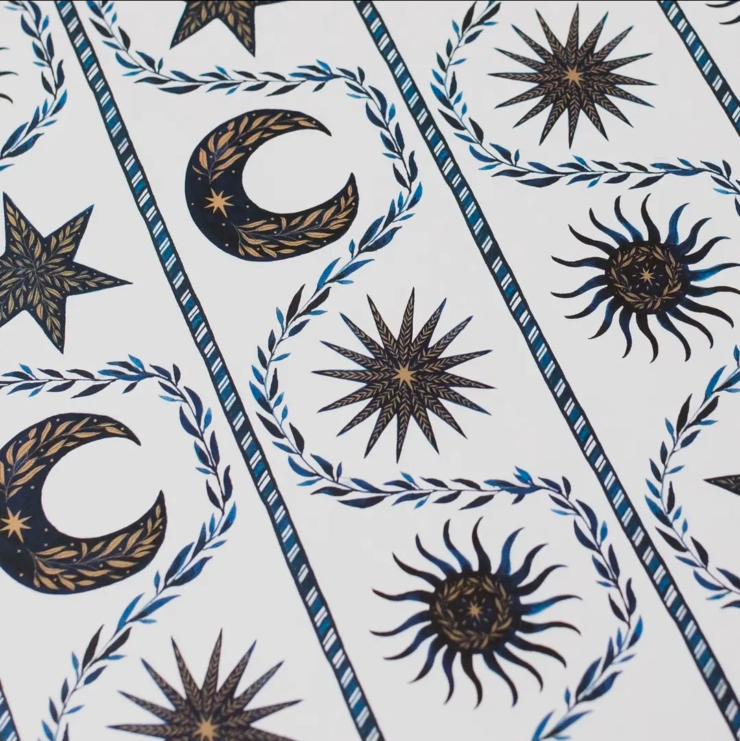 Close-up of celestial wrapping paper with navy and gold crescent moons, suns and stars between blue leafy garlands