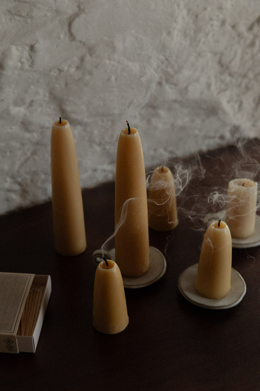 Group of beeswax candles on ceramic candle plates on a dark wooden table