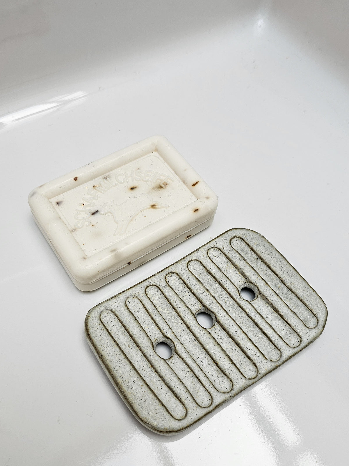 Large rustic ceramic soap dish with raised ridges and drainage holes beside a bar of handmade soap