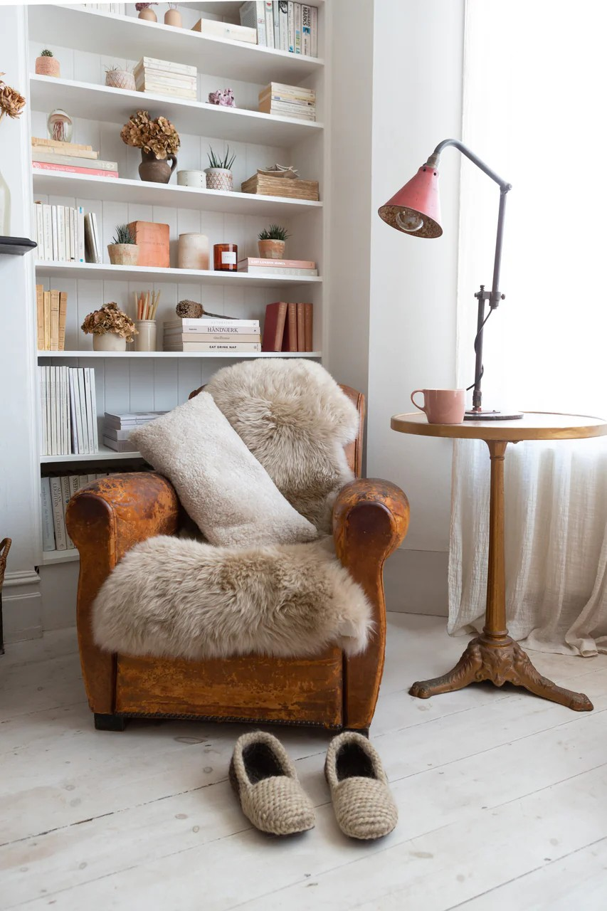 Natural sheepskin rug draped over a leather armchair beside bookshelves and a floor lamp