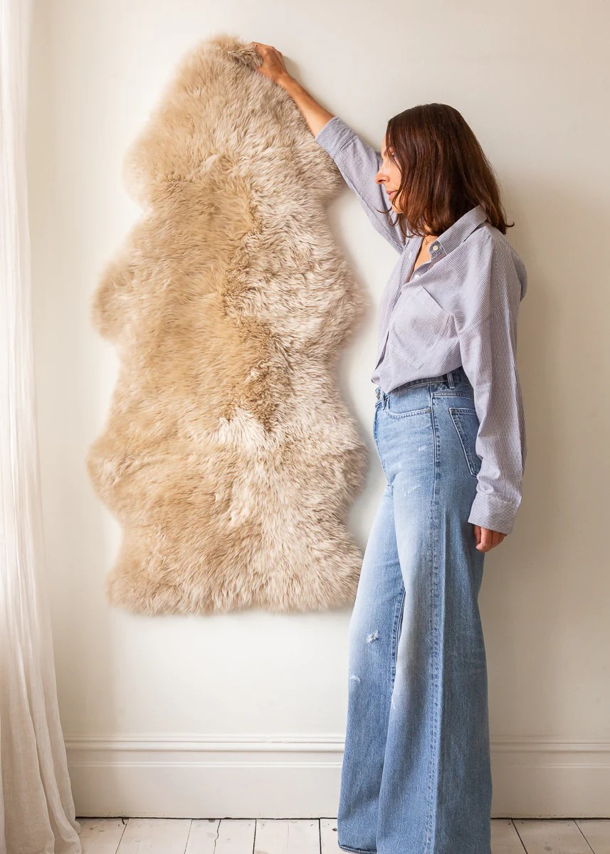 Woman holding a large double sheepskin rug against a wall to show its full length