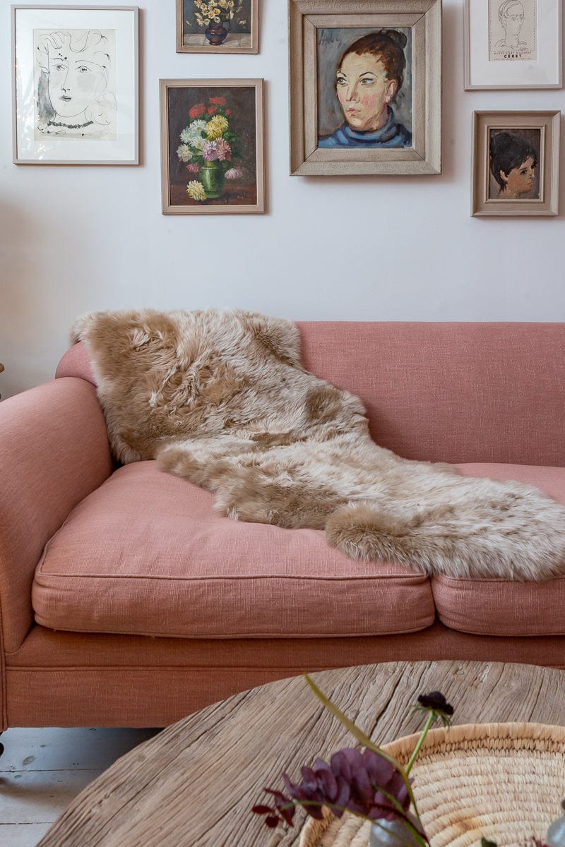 Large natural sheepskin rug draped along a pink sofa beneath a gallery wall