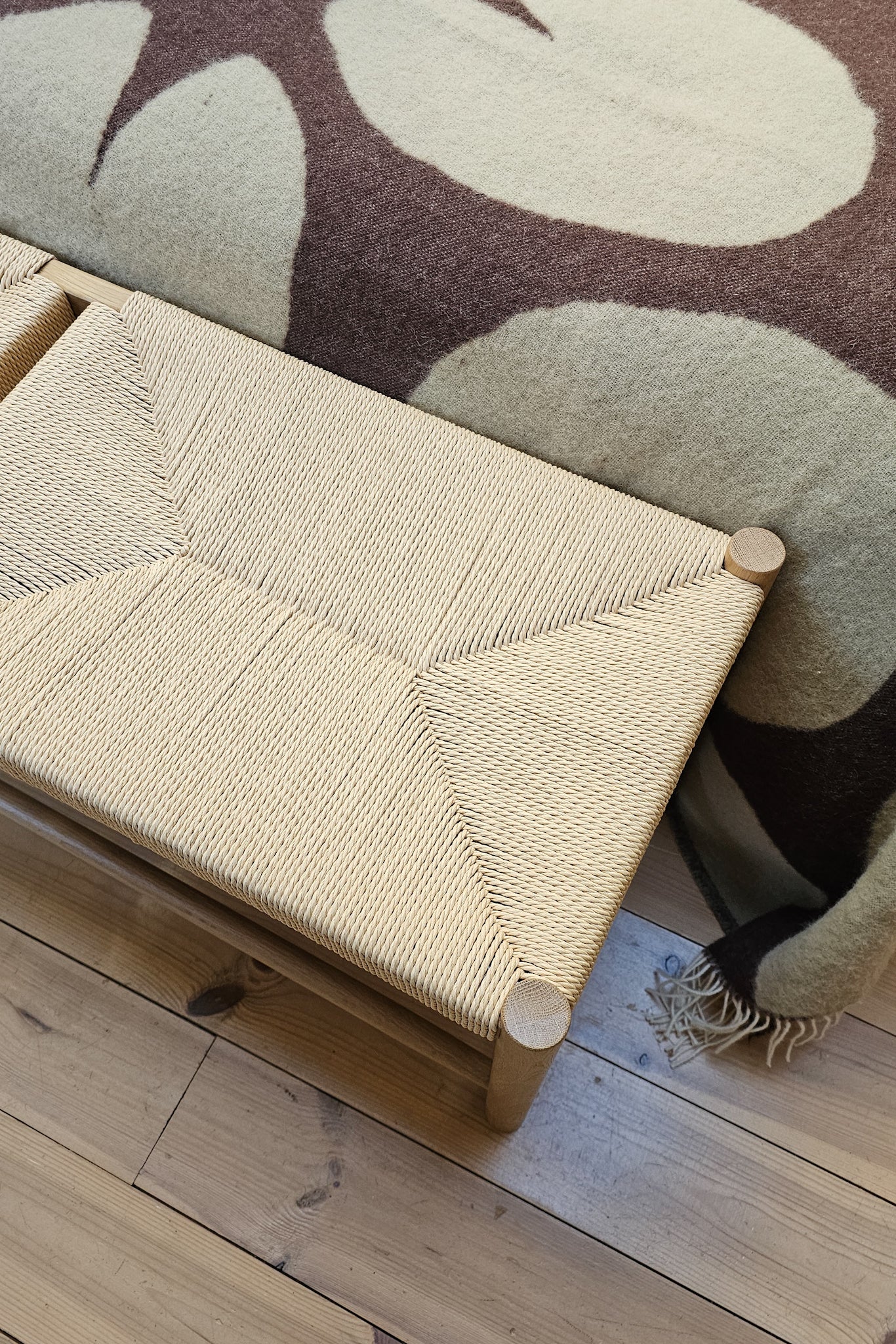 Close-up of Longworth Bench papercord weave and oak frame detail against wool throw