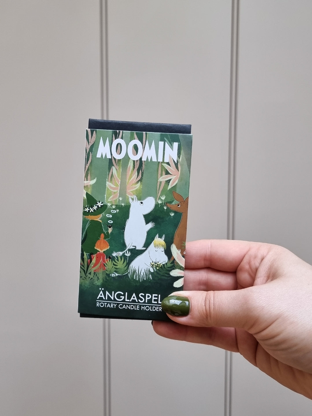 Hand holding the green illustrated Moomin Änglaspel gift box