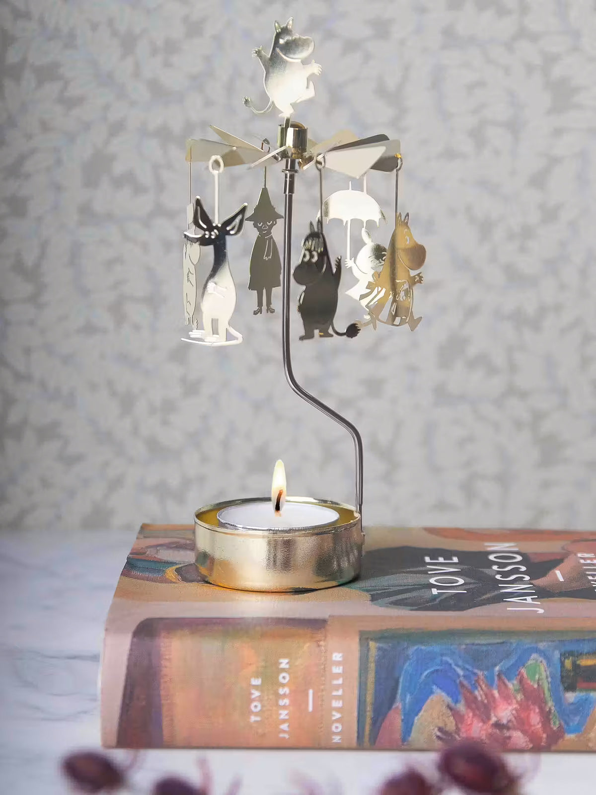 Gold Moomin Änglaspel with a lit tealight, standing on a stack of books