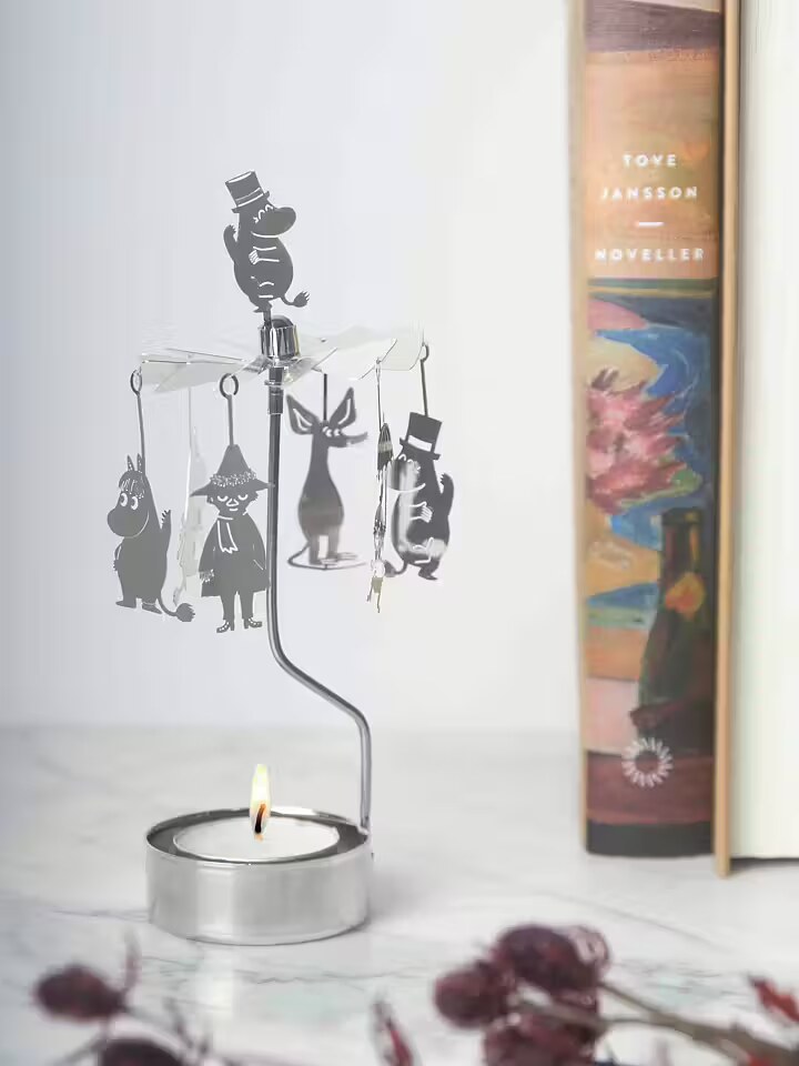 Silver Moomin Änglaspel lit on a marble surface, with Snufkin, Sniff and Moominpappa among the figures, beside a Tove Jansson book