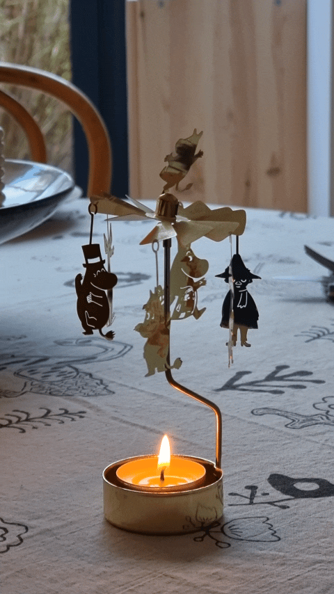 Gold Moomin Änglaspel turning above a lit tealight on a patterned tablecloth