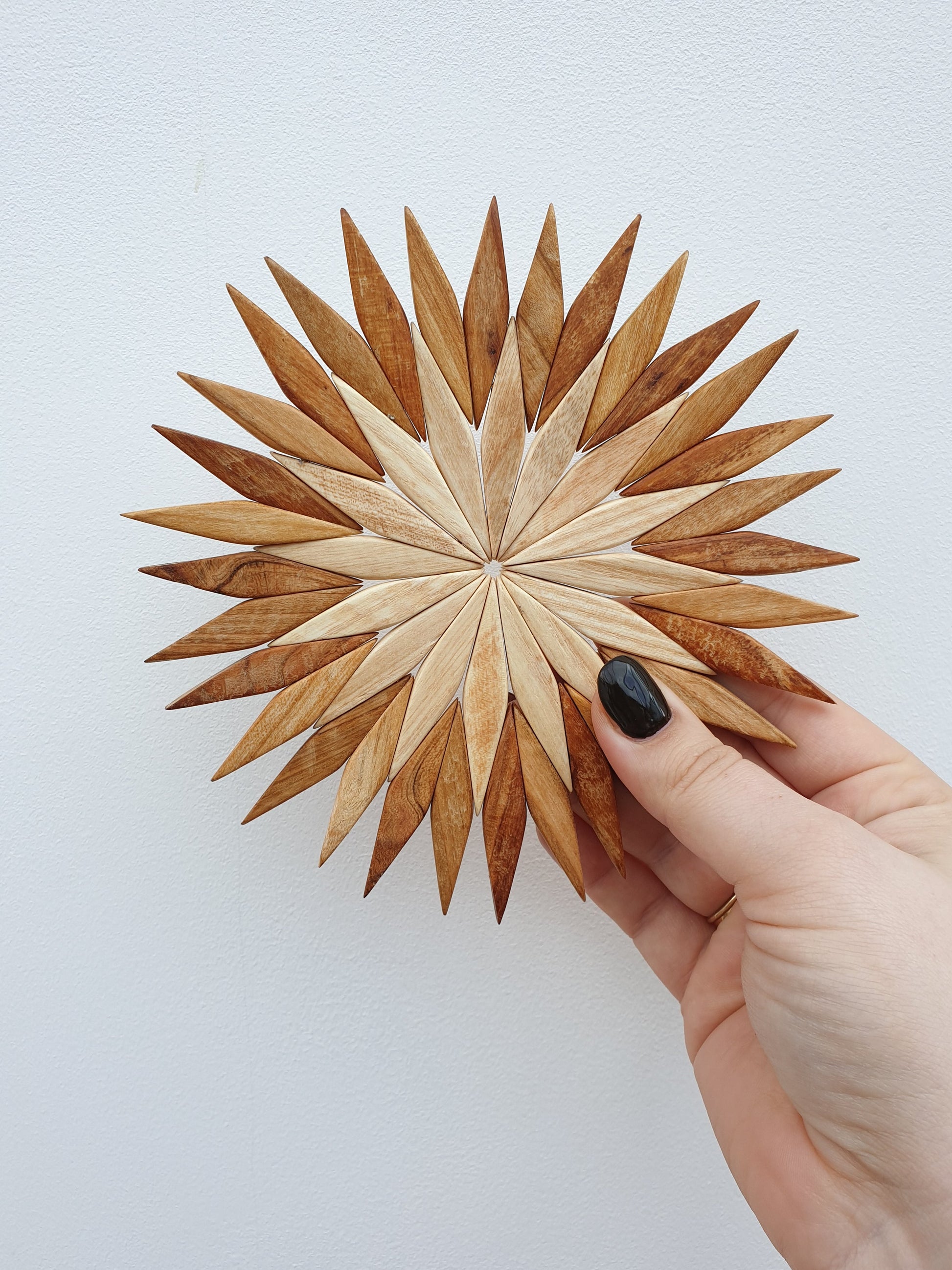 Handmade two-tone wooden starburst trivet held in hand against a white background
