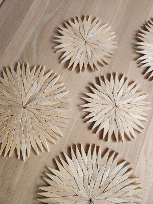 Close-up of handmade natural wooden starburst trivets showing the hand-cut pale beechwood pieces on an oak table