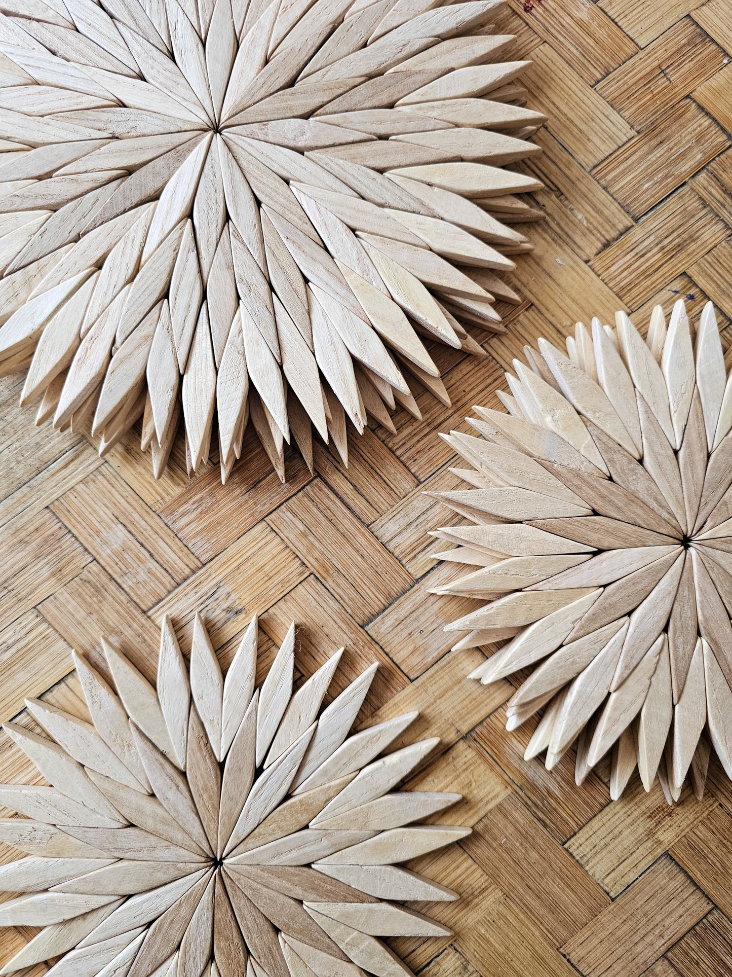 Handmade wooden starburst trivets in natural finish, shown in three sizes on a woven rattan surface in close up detail.