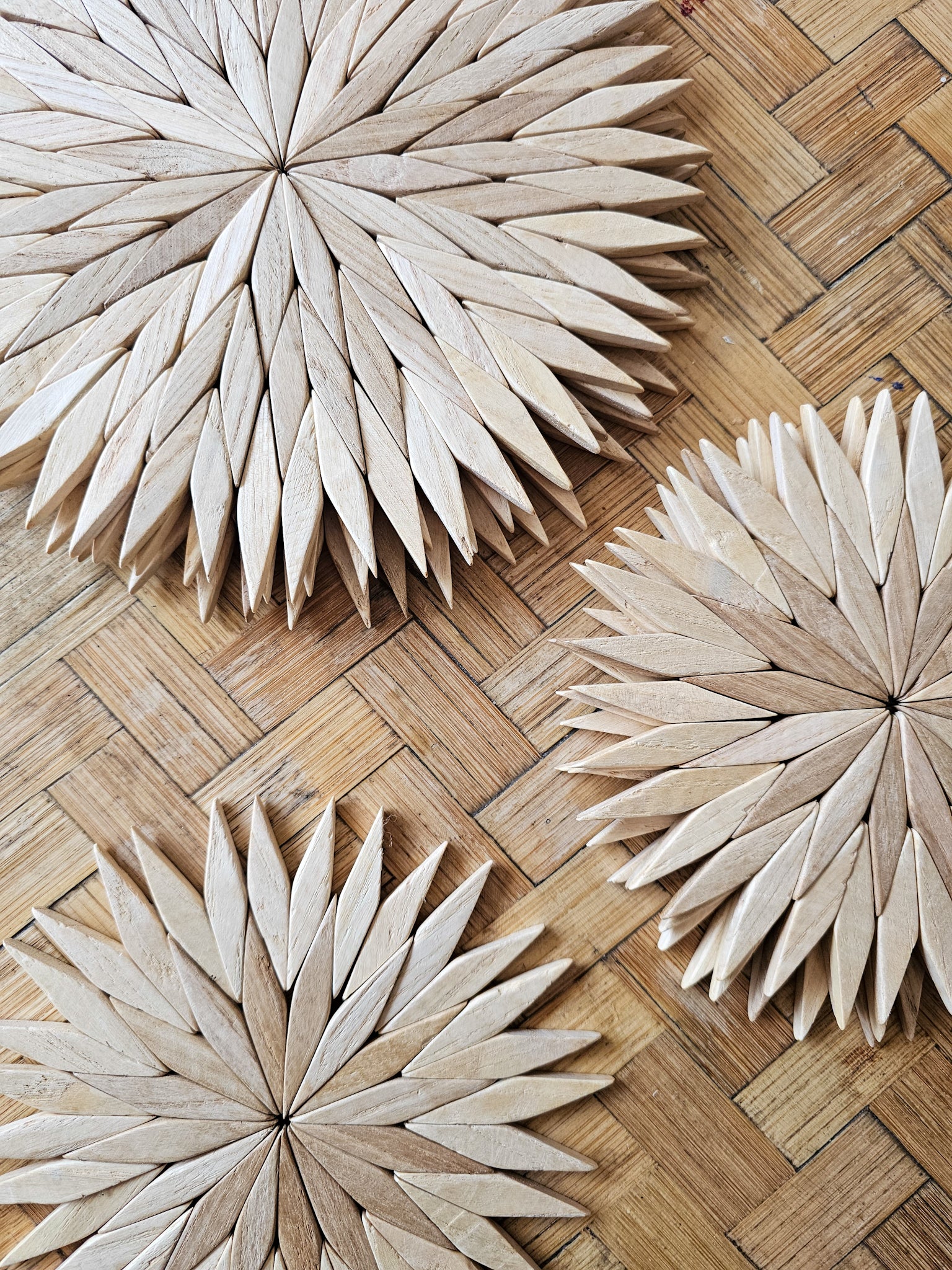 Handmade wooden starburst trivets in natural finish, shown in three sizes on a woven rattan surface in close up detail.
