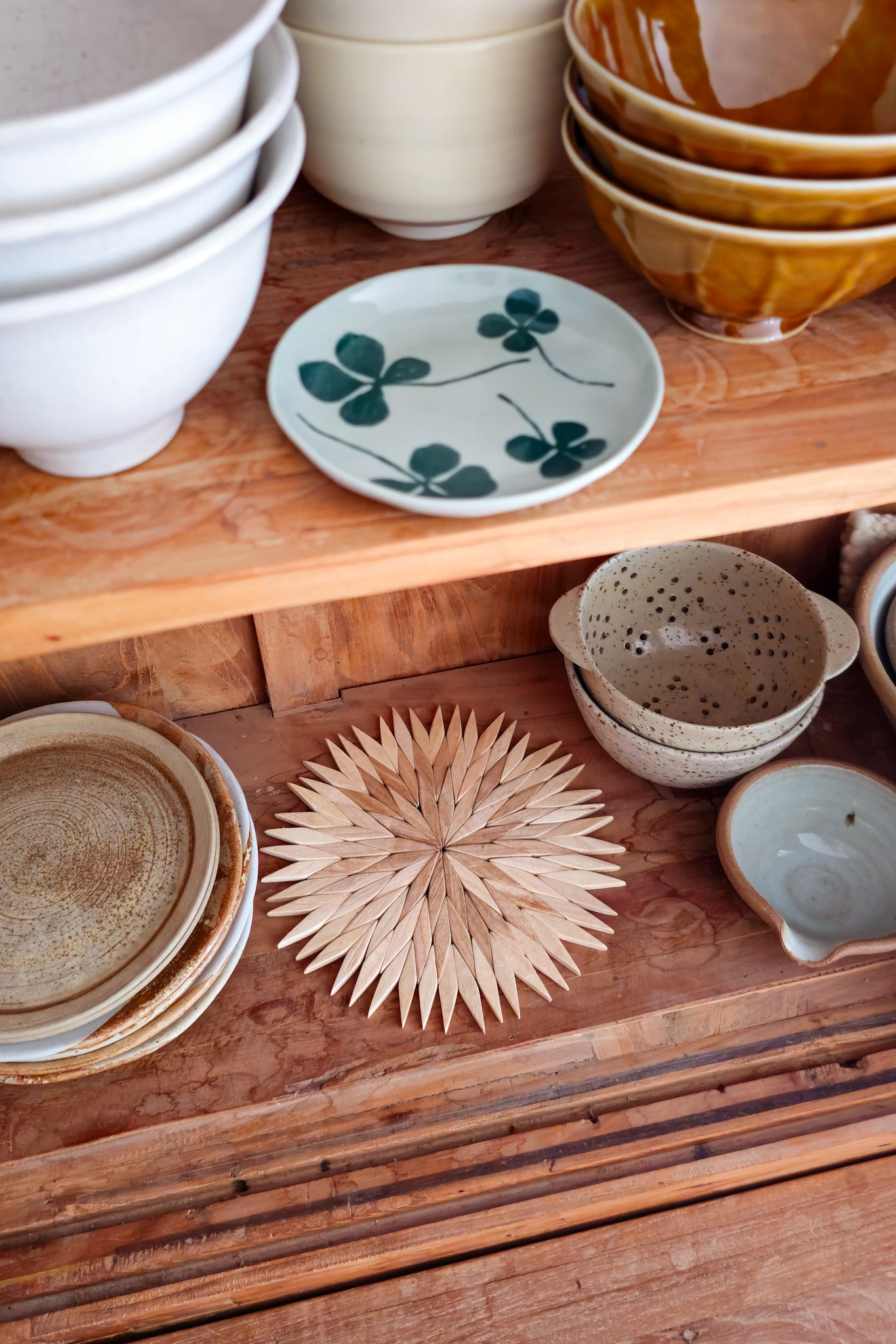 Natural wooden starburst trivet styled on a wooden shelf alongside ceramic bowls and plates