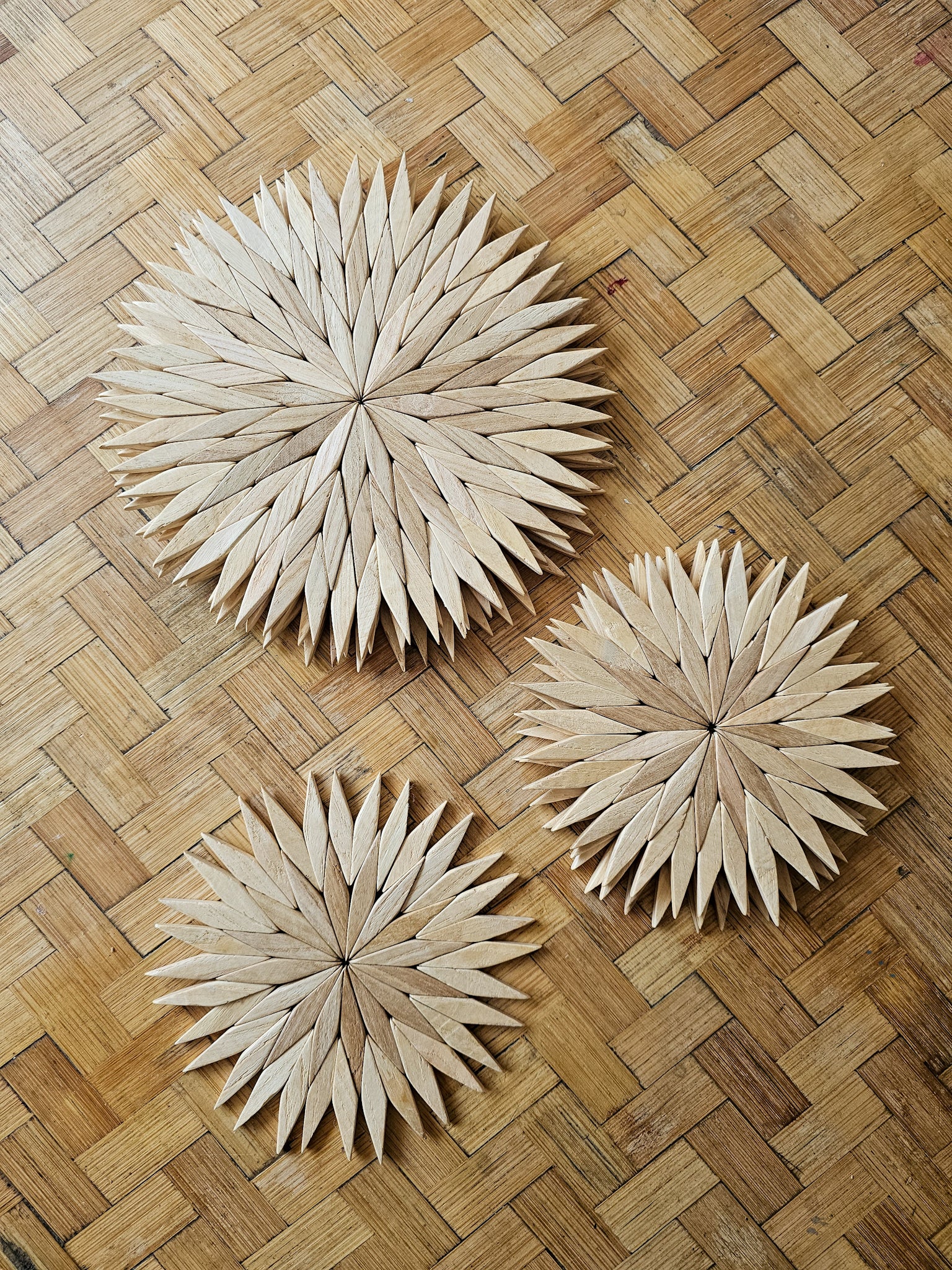 Handmade wooden starburst trivets in natural finish, shown in three sizes on a woven rattan surface
