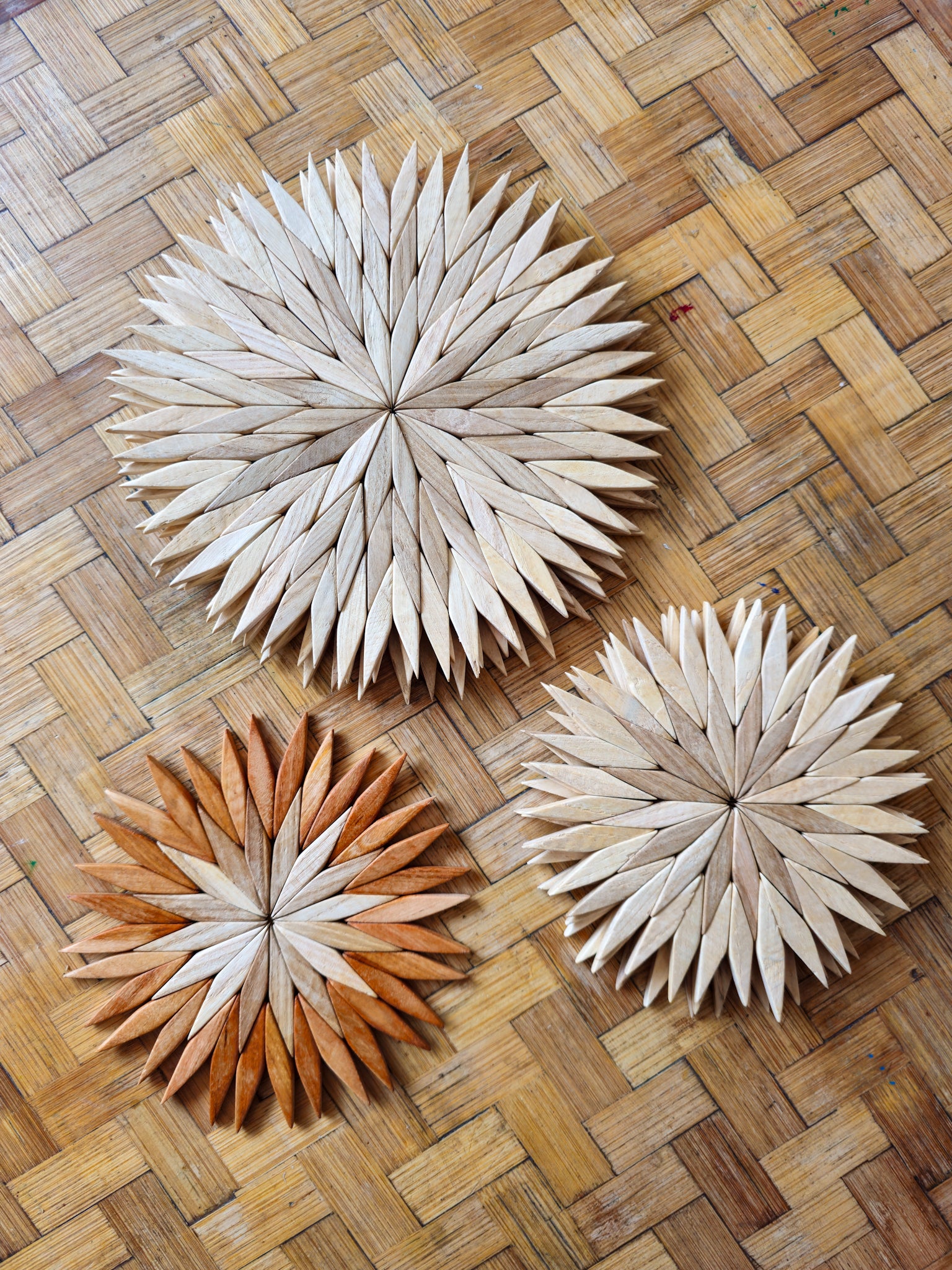 Handmade wooden starburst trivets showing natural and two-tone colourways in three sizes, on a wooden kitchen table