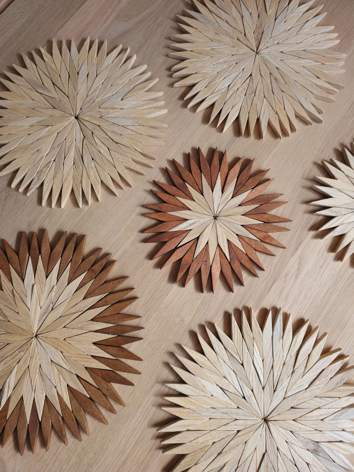 Natural and two-tone wooden starburst trivets in small and large sizes, close up on an oak table