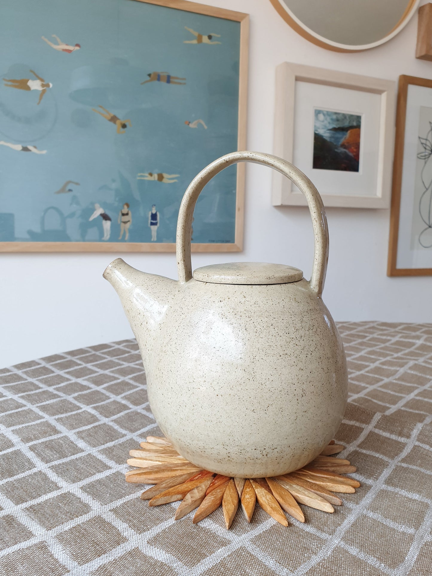 Small two-tone wooden starburst trivet used as a trivet under a speckled ceramic teapot on a linen tablecloth