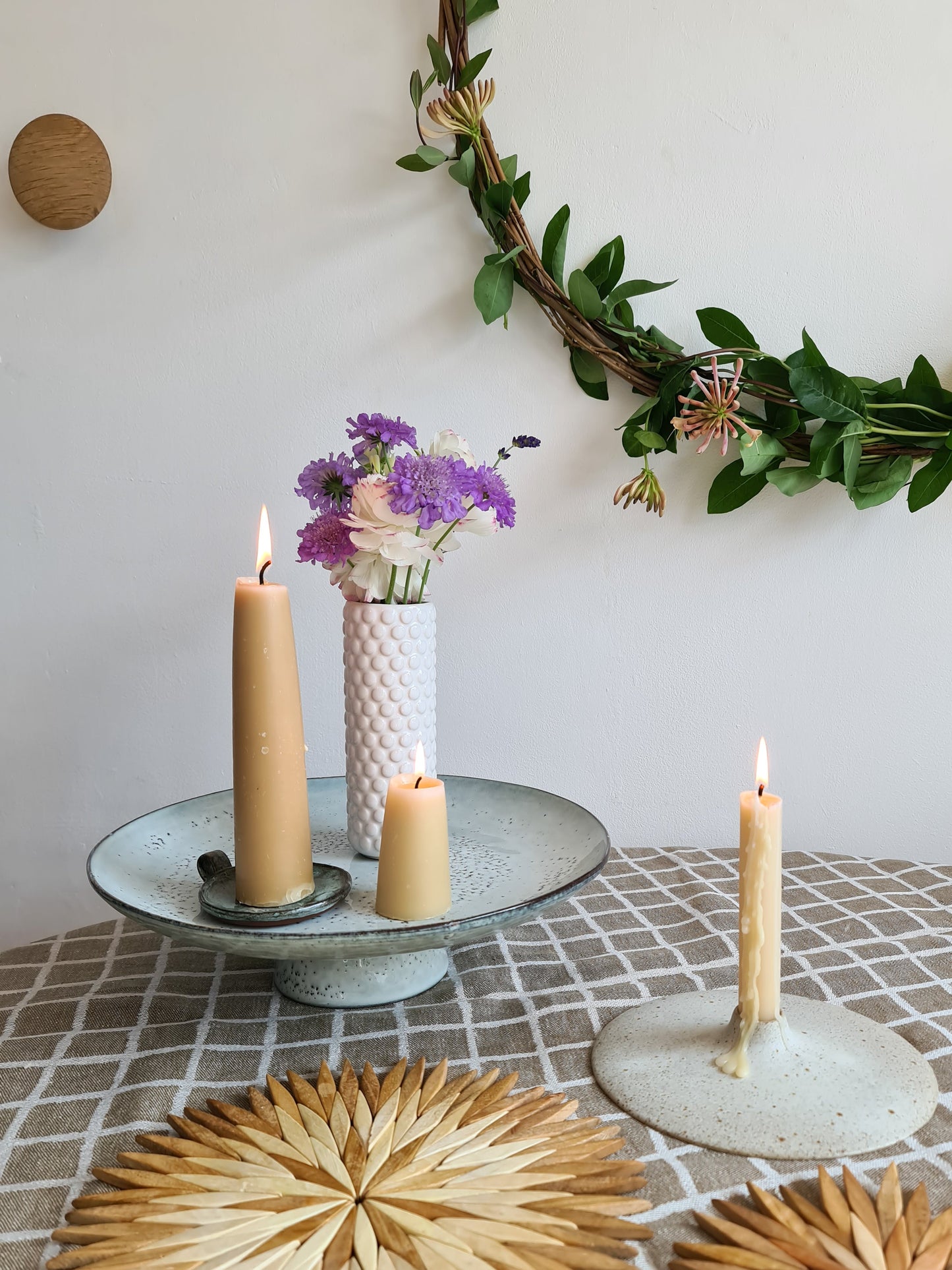 Natural wooden starburst trivets used as placemats on a linen tablecloth, styled with beeswax candles, ceramic cake stand and fresh flowers