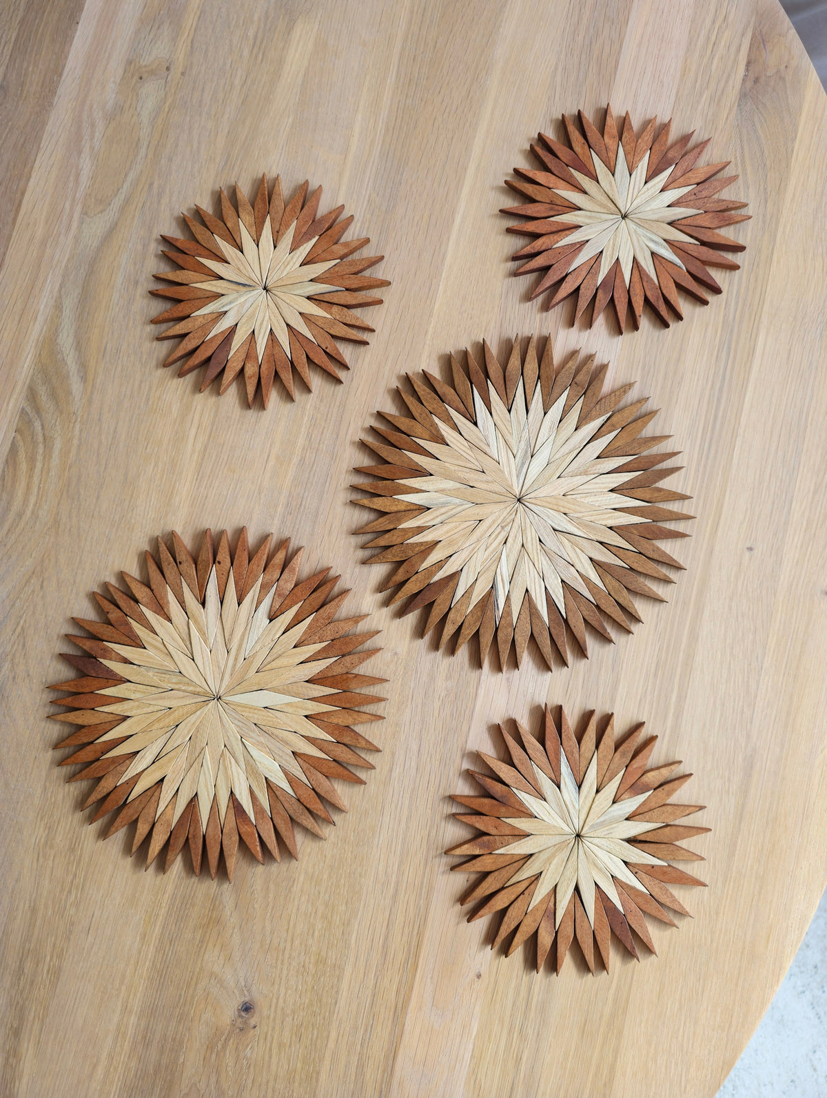 Five handmade two-tone wooden starburst trivets in small and large sizes laid out on a round oak table