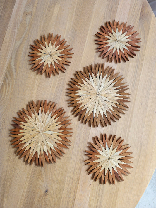Five handmade two-tone wooden starburst trivets in small and large sizes laid out on a round oak table