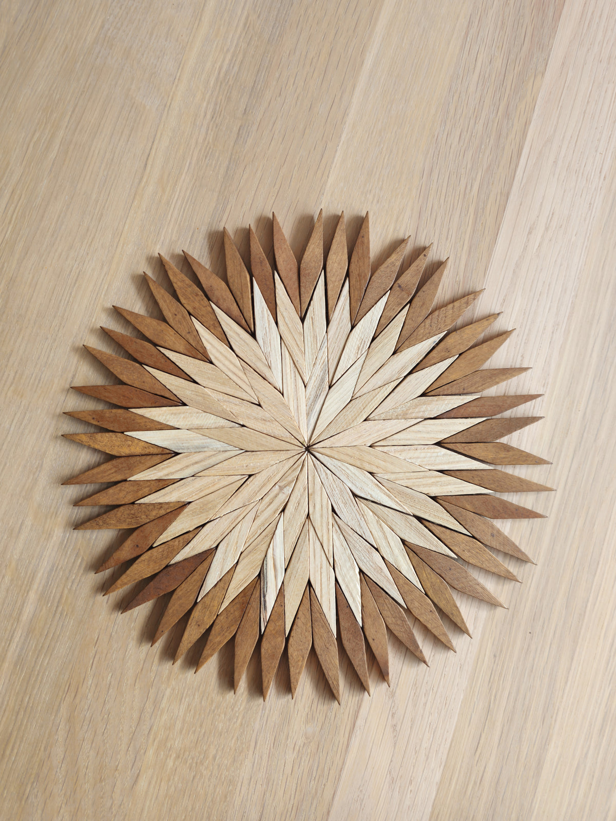 Large two-tone wooden starburst trivet in Carpathian beechwood, with a pale centre and warm brown outer petals, on an oak table