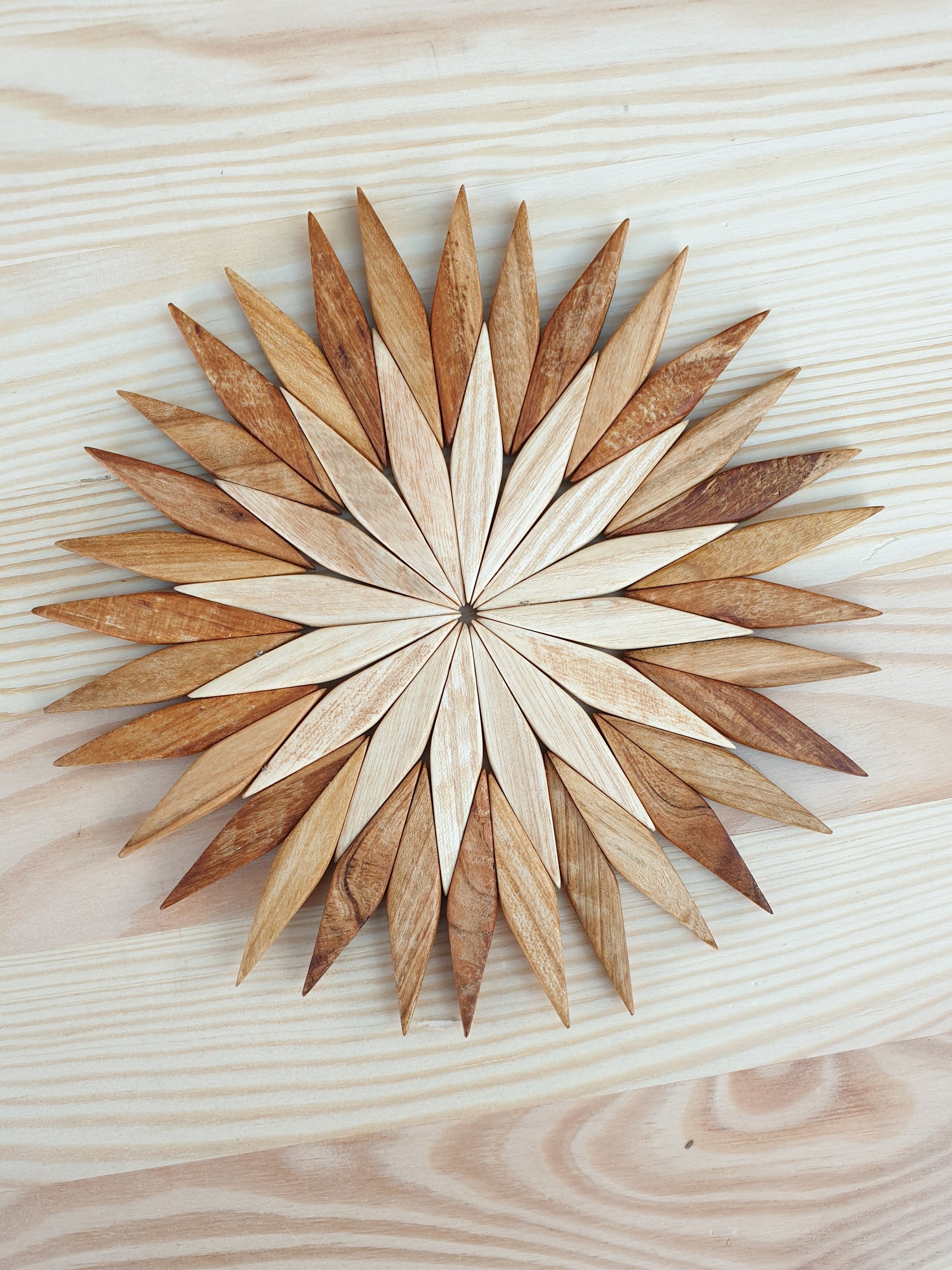 Large two-tone wooden starburst trivet photographed from above on a pale wood surface, showing handcrafted detail