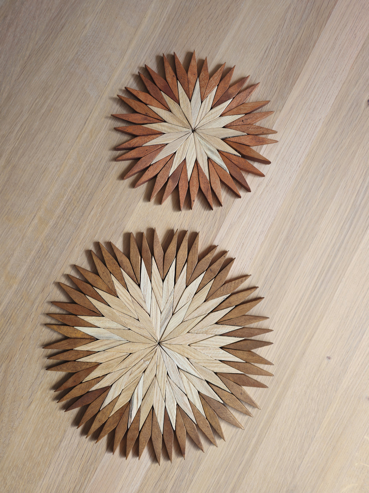 Small and large two-tone wooden starburst trivets side by side on an oak table