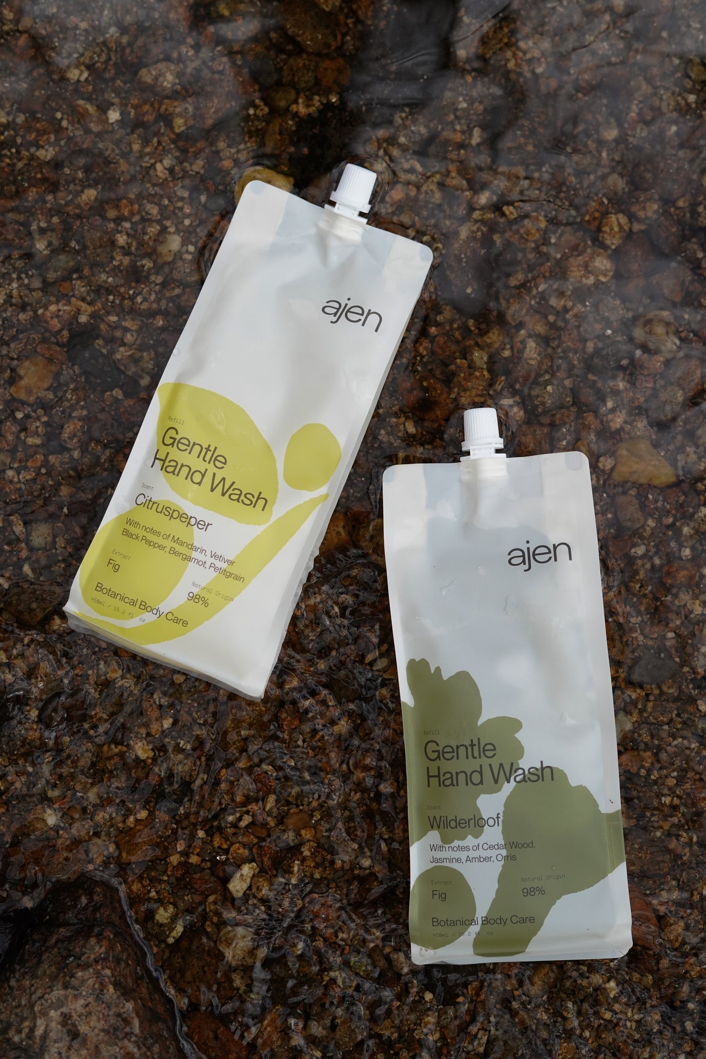 Two Ajen gentle hand wash refill pouches, one Wilderloof and one Citruspeper laid down on a natural water source.