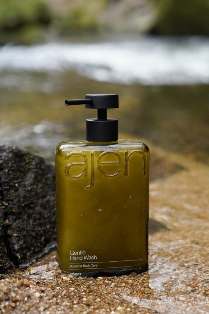 Ajen gentle hand wash pump glass bottle sat on a natural water source.