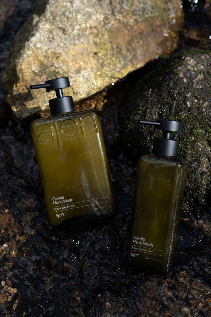 Two pump bottles of Ajen hand wash placed on a natural stone surface.