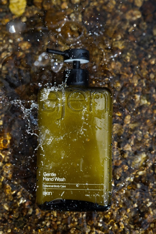 Ajen hand wash glass bottle placed on a natural water surface with water caugh mid motion splashing it.