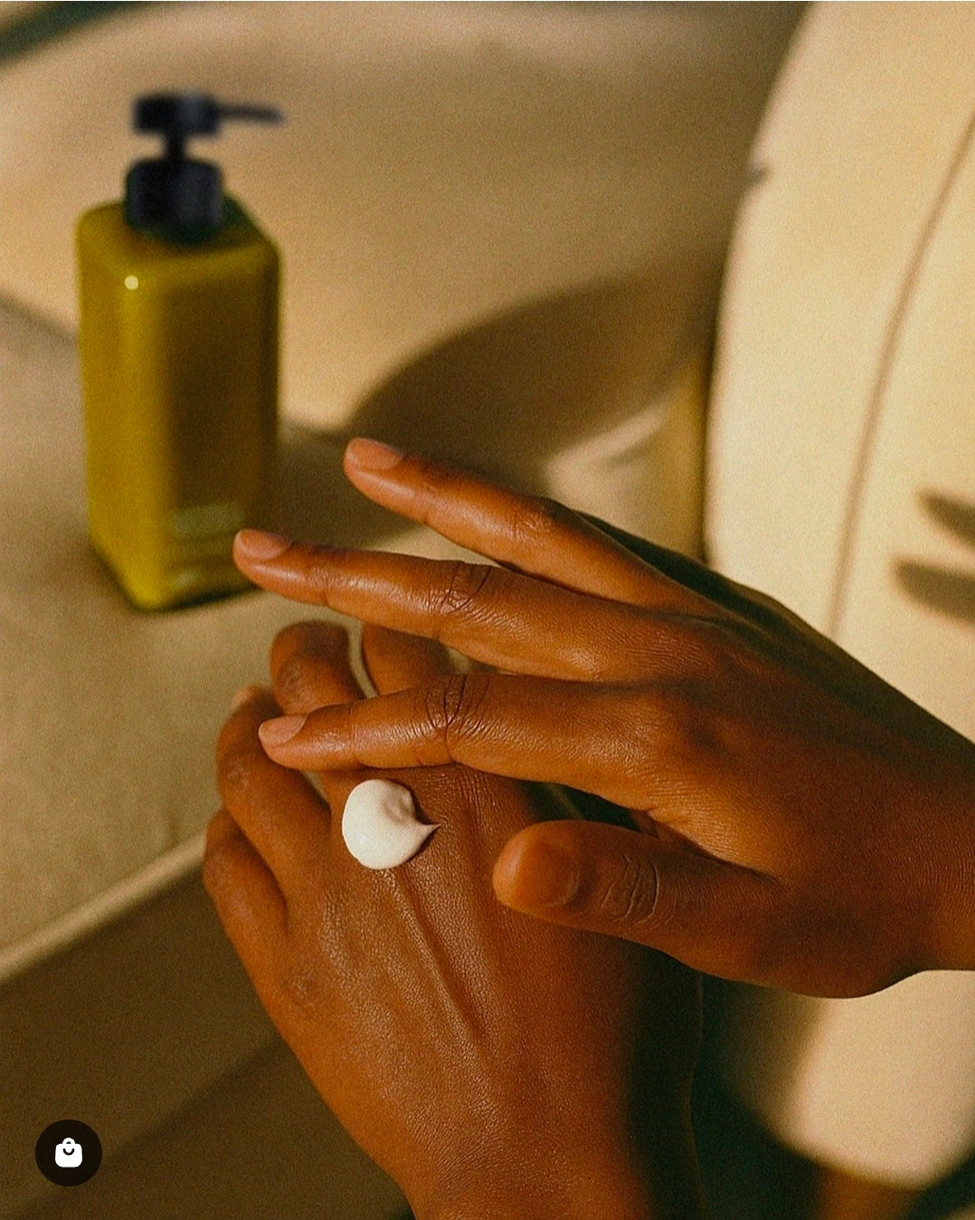 Two hands applying Ajen handbalm with the glass bottle in the background.
