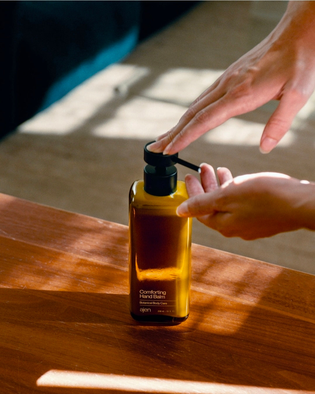 Hand applying balm from a glass bottle on a wooden surface.