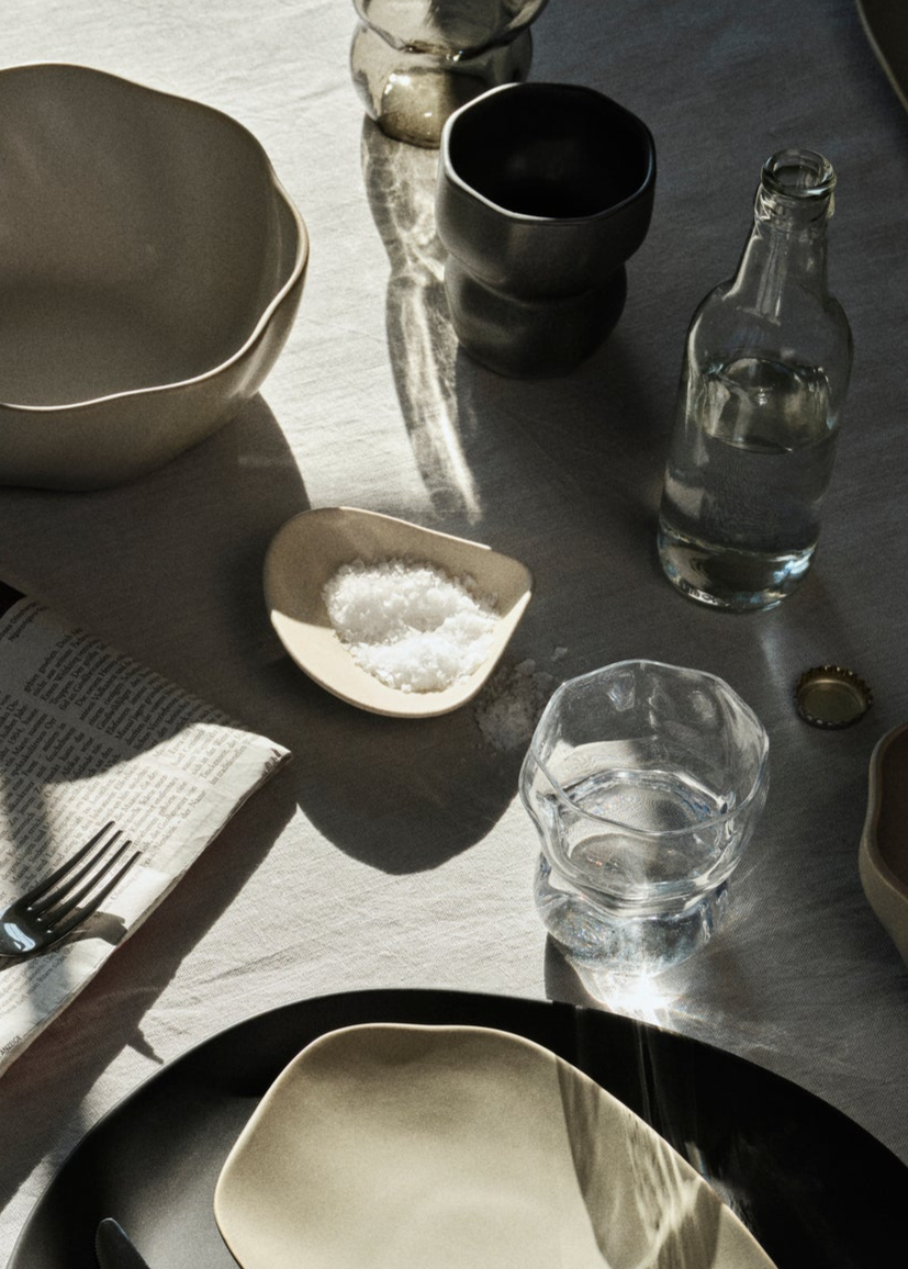 Dining table setting with ceramic bowls, glassware, and a salt cellar.