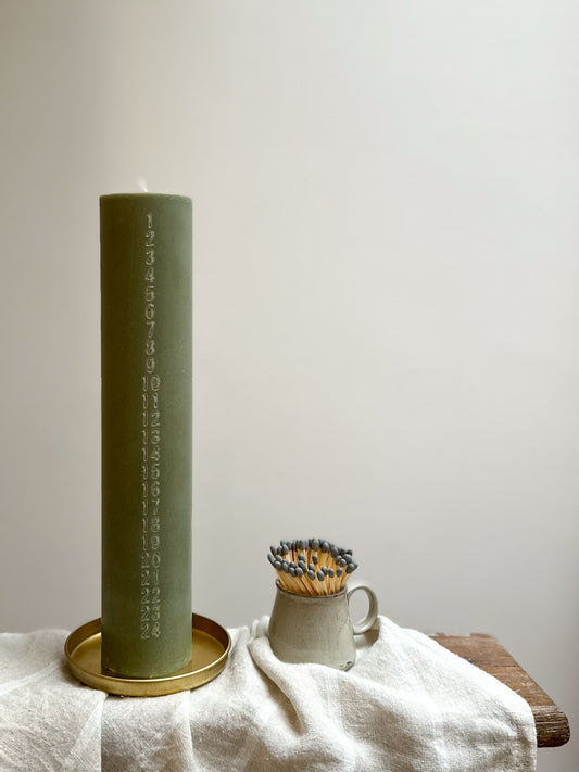 Green candle on a gold tray with a white cloth and wooden surface in the background