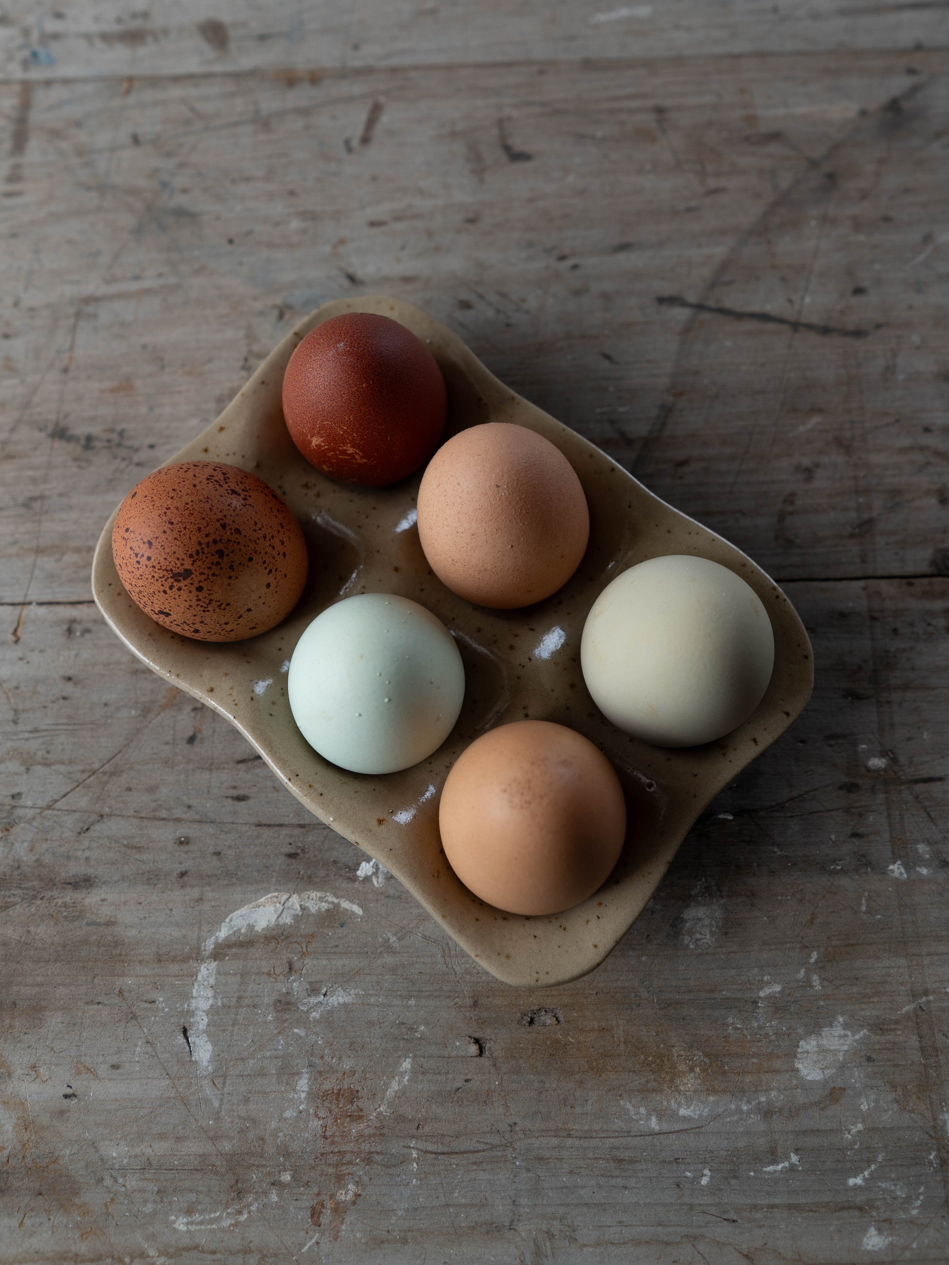 A variety of eggs with different colors and patterns placed in a stoneware egg tray on a wooden surface.