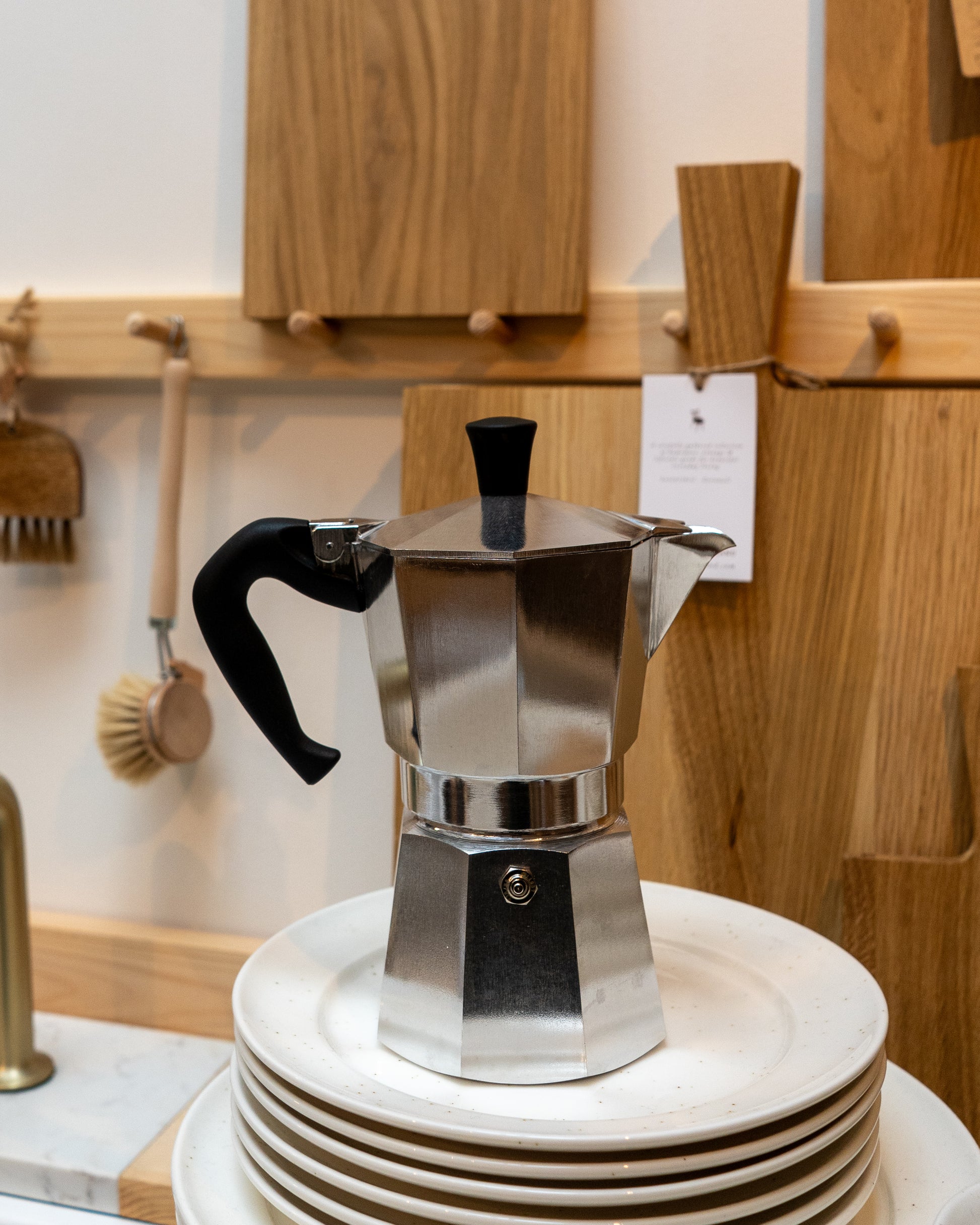 Stainless steel Moka pot on a stack of white plates with wooden cabinets in the background