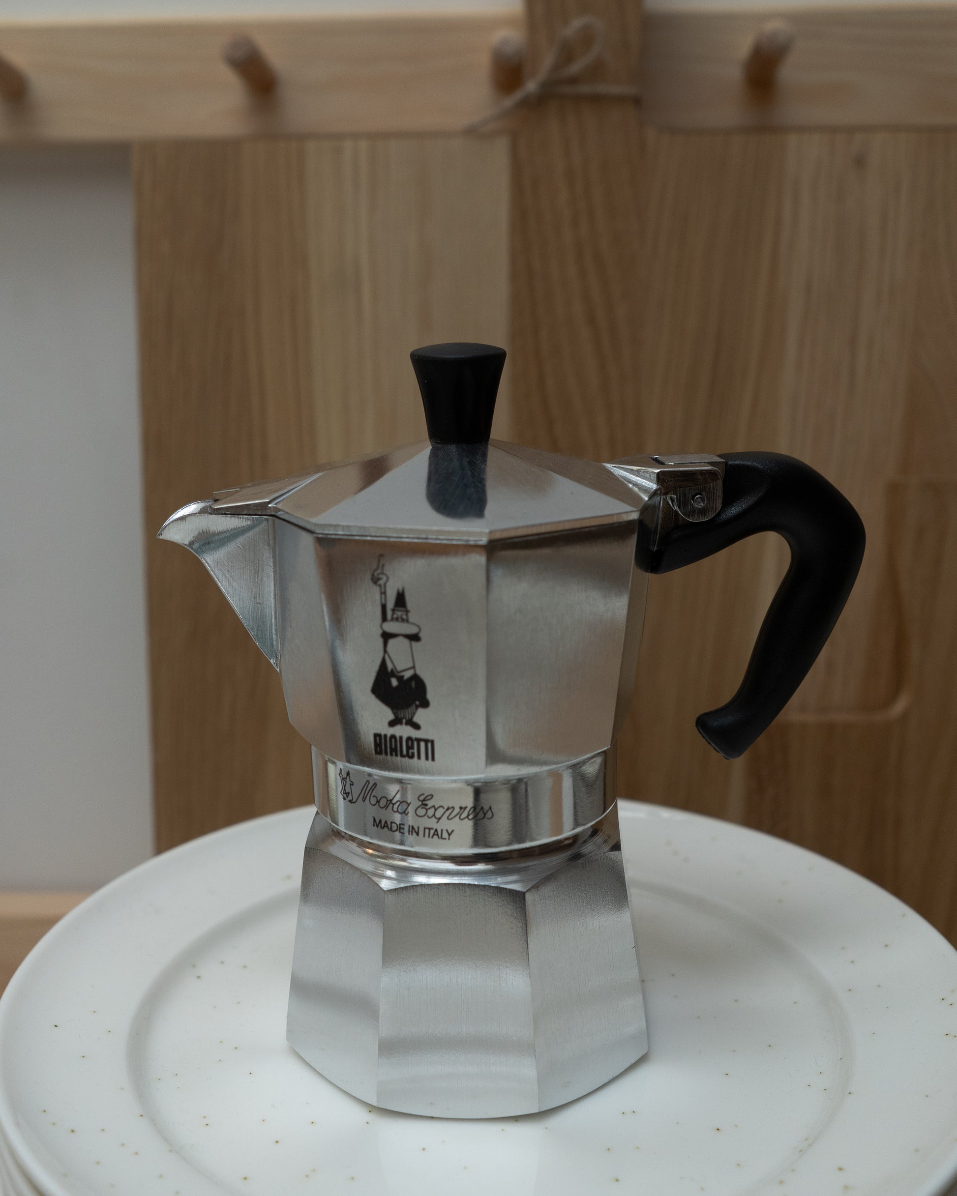 Silver Bialetti coffee maker on a white plate with a wooden background